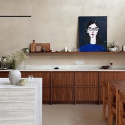 Madde studio Sp. z o.o. - Nowoczesna kuchnia z drewnianymi szafkami, marmurowym blatem i wyspą. Na ścianie obraz z portretem kobiety. Minimalistyczne oświetlenie i dekoracje.