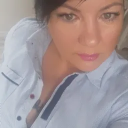 Portret kobiety z krótkimi, ciemnymi włosami, w bluzce w paski. Widoczne delikatne zmarszczki mimiczne wokół oczu i tatuaż na dekolcie. Ujęcie z góry.