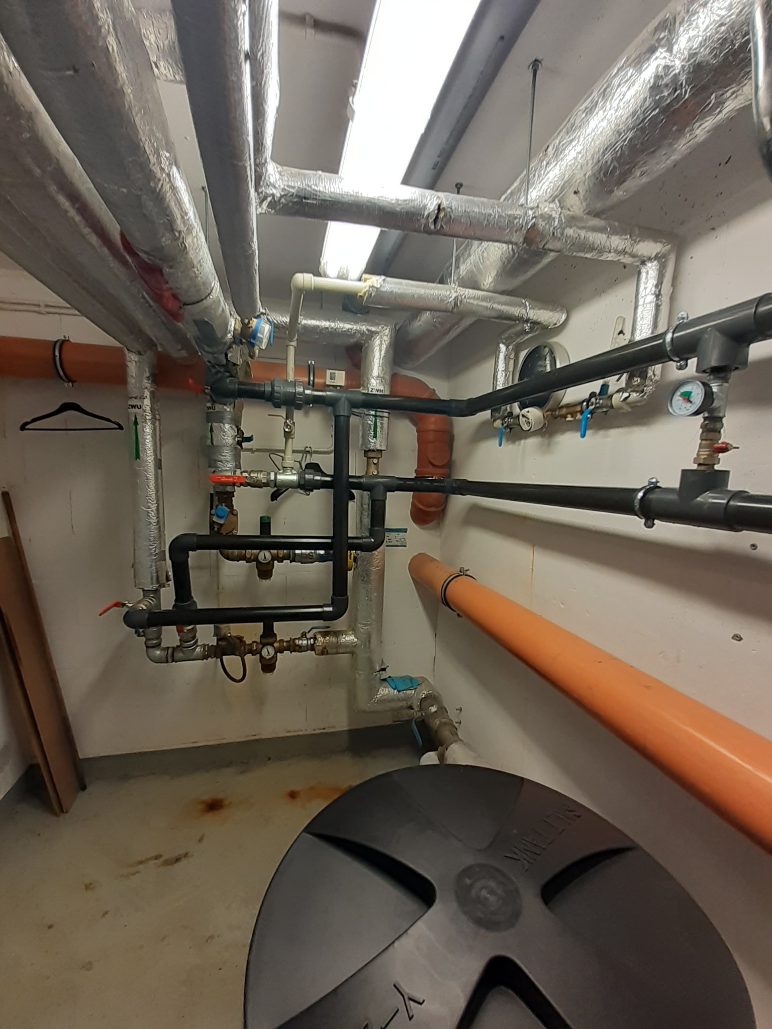 Kompaktowa kotłownia z rurami w izolacji, licznymi zaworami, manometrami i elementami instalacji, widoczny zbiornik z napisem SALT TANK.