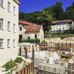 Elektro -Tech - Budowa fundamentów budynku z widocznymi elementami konstrukcyjnymi, rusztowaniami i zabezpieczeniami wykopu; w tle budynki mieszkalne i drzewa.