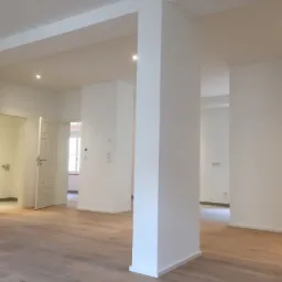 Nowoczesne, przestronne wnętrze z drewnianą podłogą i białymi ścianami, oświetlone punktowymi lampami sufitowymi, ukazujące efekt po instalacji elektrycznej.