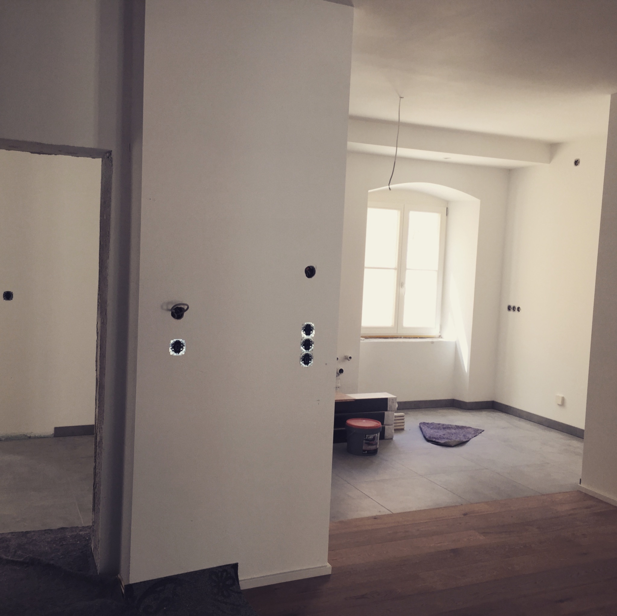 Wnętrze w trakcie remontu, widoczne puszki instalacyjne na ścianie, surowe wykończenie, przygotowanie do montażu osprzętu elektrycznego, podłoga częściowo wyłożona płytkami, częściowo drewniana...