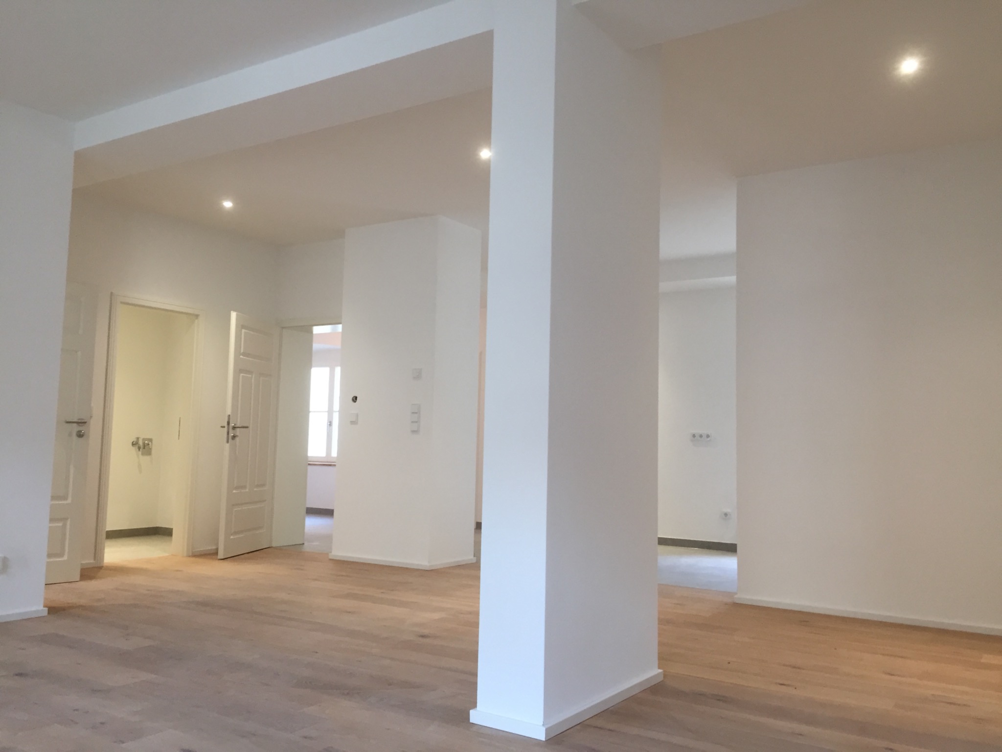 Nowoczesne, przestronne wnętrze z drewnianą podłogą i białymi ścianami, oświetlone punktowymi lampami sufitowymi, ukazujące efekt po instalacji elektrycznej.