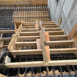 Szczegółowy widok z góry na szalunek schodów zbrojonych, z widoczną siatką zbrojeniową i deskami szalunkowymi, przygotowany do zalania betonem.