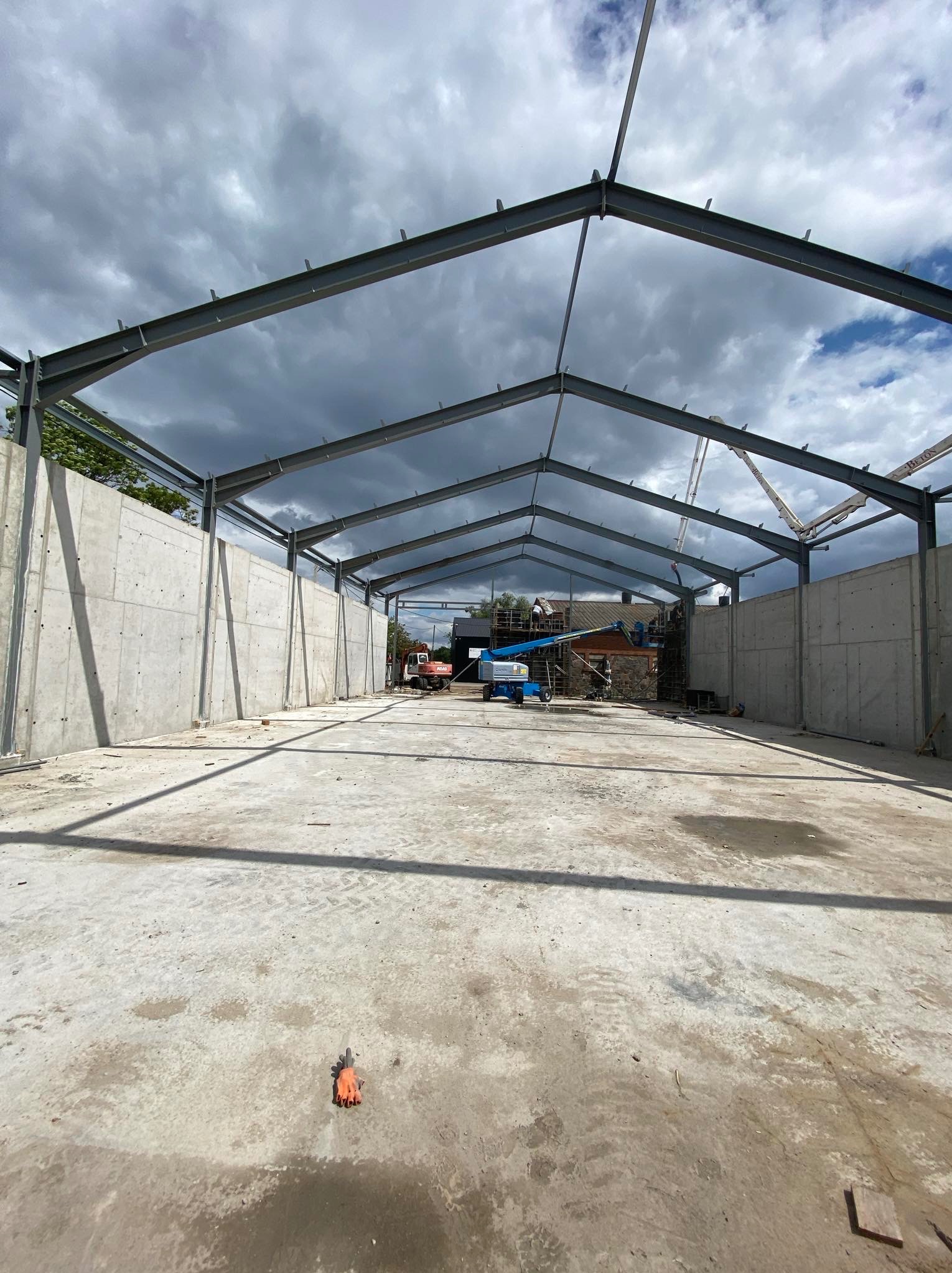 Konstrukcja hali z betonu i stali w Kutnie, widok wnętrza. Na pierwszym planie betonowa posadzka, w tle maszyny budowlane i pochmurne niebo.