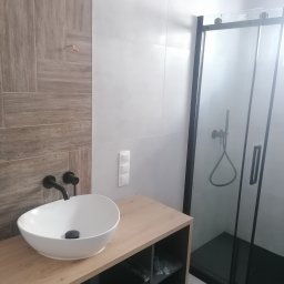 Wajmar - Nowoczesna łazienka z umywalką nablatową, czarną armaturą, kabiną prysznicową typu walk-in z czarnymi profilami i płytkami imitującymi drewno na ścianie.