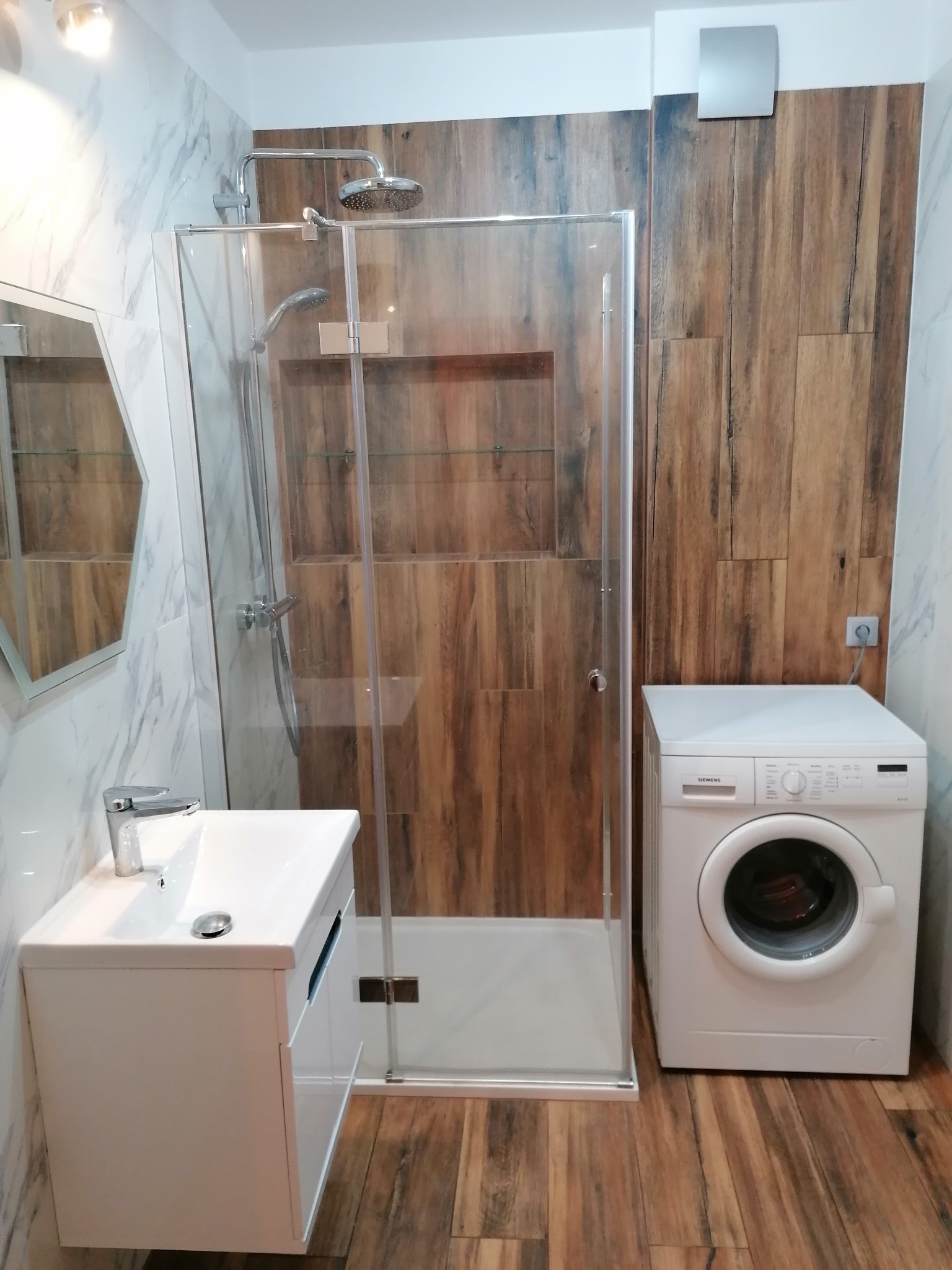 Nowoczesna łazienka z kabiną prysznicową, umywalką na szafce i pralką Siemens, wykończona płytkami imitującymi drewno i marmur.