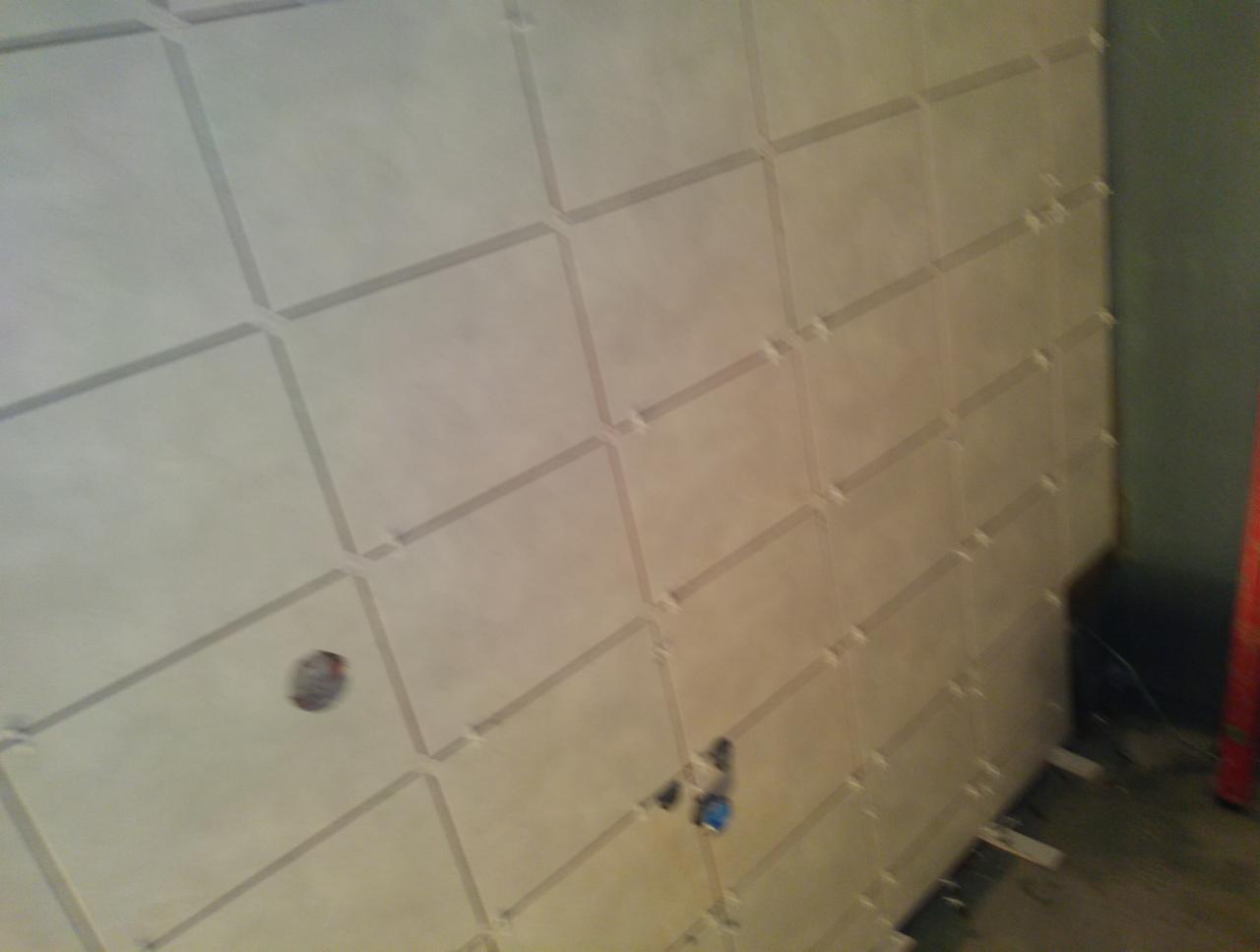 Ściana pokryta beżowymi płytkami ceramicznymi ułożonymi w regularny wzór z widocznymi krzyżykami dystansowymi, w trakcie układania płytek w pomieszczeniu.