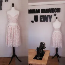 Koronkowy, dwuczęściowy komplet w odcieniach pudrowego różu na manekinie, obok zabytkowa maszyna do szycia i napis 'Zakład Krawiecki u Ewy' na białej ceglanej ścianie.