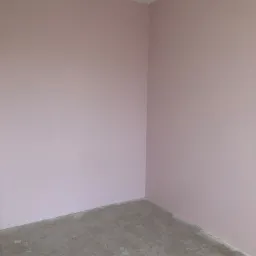 Świeżo pomalowany róg pokoju na pudrowy róż, surowy beton na podłodze, widoczny pojemnik z resztkami farby.