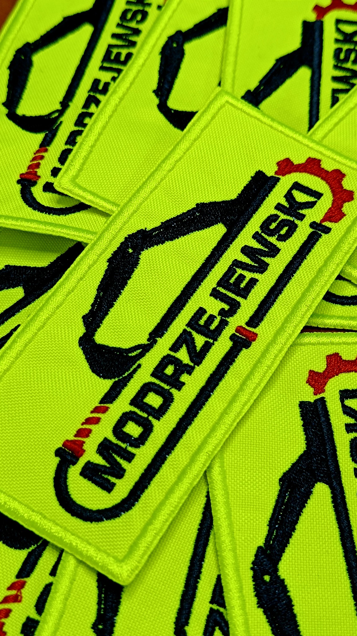 Żółte naszywki z haftowanym czarnym rysunkiem koparki i czerwonym kołem zębatym oraz napisem 'MODRZEJEWSKI'