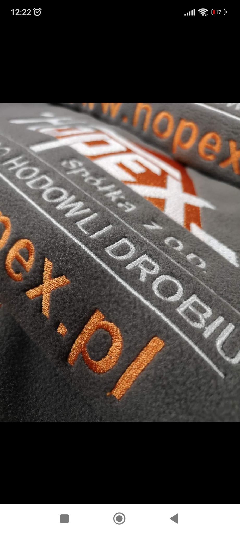 Szary materiał z pomarańczowo-białym haftem przedstawiającym nazwę firmy 'HODOWLI DROBIU' oraz adres strony internetowej.