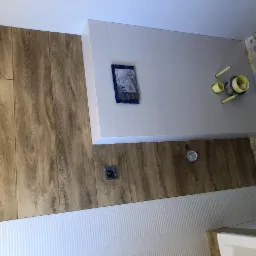 Montaż okładziny ściennej imitującej drewno w łazience, widoczne przyłącza hydrauliczne i częściowo wykończona ściana z białymi panelami.