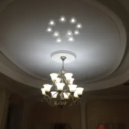 Ozdobny sufit z gipsowymi sztukateriami i żyrandolem z mlecznymi kloszami, widoczne również ślady po pracach wykończeniowych na ścianach.