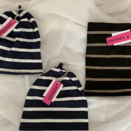 Trzy paski dzianiny: dwie granatowo-białe czapki z etykietami ZUZOLA i czarno-beżowy komin na białym, lekko pogniecionym tle.