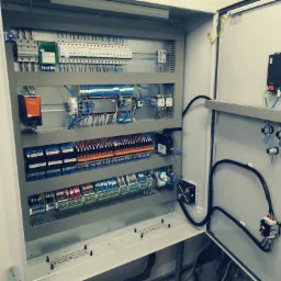 Otwarta szafa sterownicza z licznymi przewodami, bezpiecznikami i modułami, widoczne staranne ułożenie przewodów i elementów.