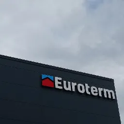 Elewacja budynku z logo firmy Euroterm, widoczne szare panele elewacyjne i pochmurne niebo w tle.