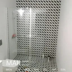 Nowoczesna łazienka z kabiną prysznicową i toaletą, wykończona czarno-białymi płytkami o geometrycznym wzorze 3D, widoczny fragment ściany z datą i godziną nałożoną przez aplikację.