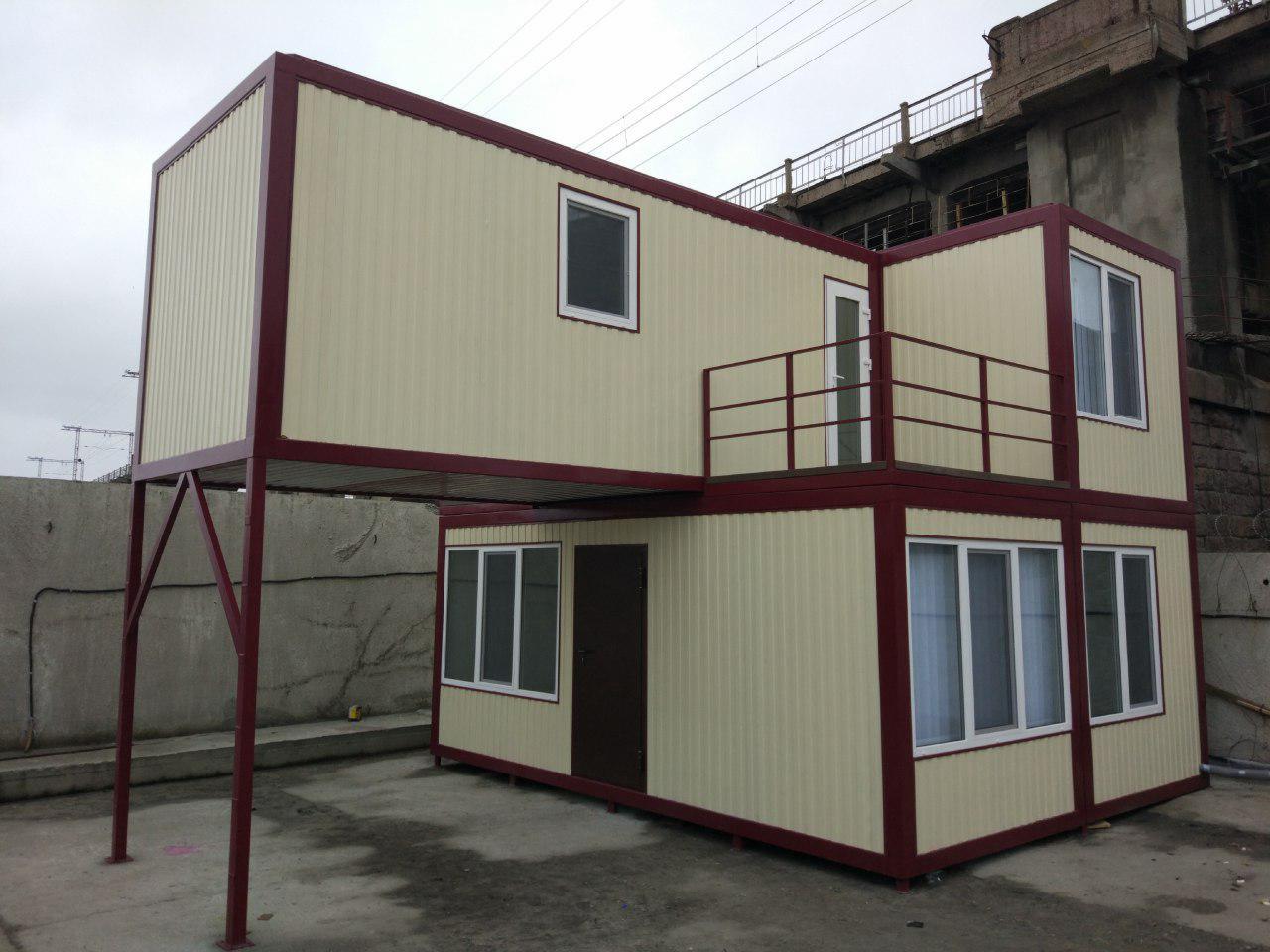 Dwukondygnacyjny dom modułowy z beżowych paneli z bordowymi obramowaniami, wsparty na stalowej konstrukcji, balkon z bordową barierką na górnej kondygnacji.