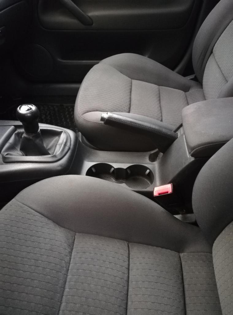 Wnętrze samochodu z szarą tapicerką materiałową, widoczny fotel kierowcy, dźwignia zmiany biegów i hamulec ręczny.