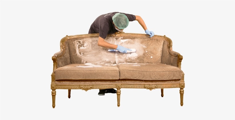 Pracownik w czepku i rękawicach czyści szczotką zabrudzoną, brązową kanapę w stylu vintage, widoczna piana czyszcząca.