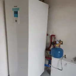 Biała pompa ciepła Panasonic zainstalowana w pomieszczeniu w Wiślince, widoczne rury i osprzęt hydrauliczny.