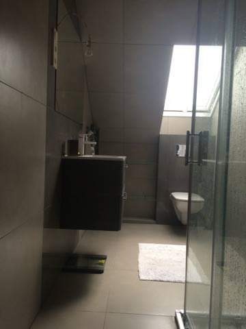 Nowoczesna łazienka w szarościach z kabiną prysznicową typu walk-in, wiszącą szafką z umywalką, lustrem, toaletą i oknem dachowym