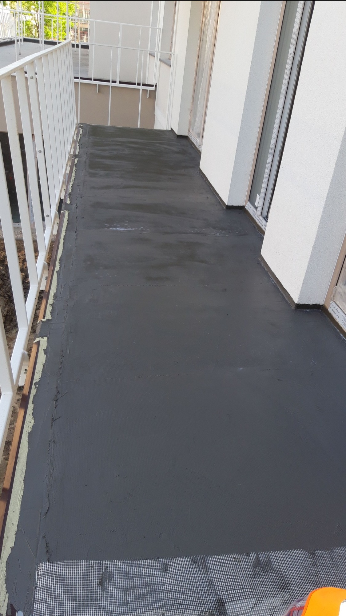 Balkon w trakcie hydroizolacji z użyciem szarej masy Aquafin, widoczna siatka wzmacniająca na krawędzi.