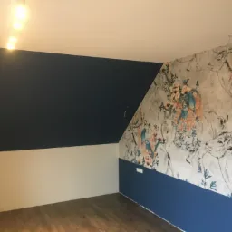 Pokój na poddaszu po odświeżeniu: ściany pomalowane w dwóch odcieniach, górna część granatowa, dolna kremowa, jedna ściana pokryta tapetą w motywy zwierzęce i roślinne, drewniana podłoga.