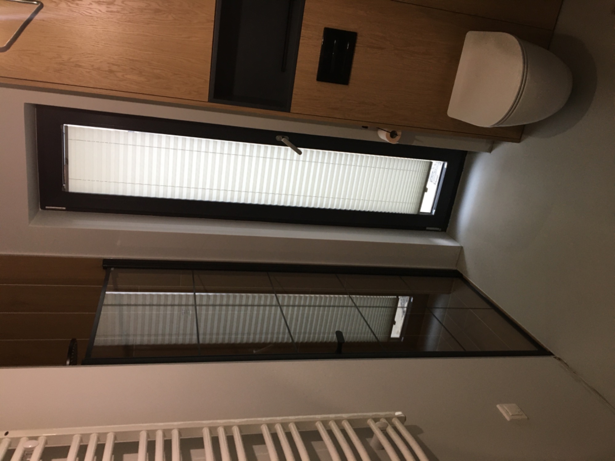 Nowoczesna łazienka z drewnianymi szafkami, roletami w oknach i grzejnikiem drabinkowym; widok z góry.