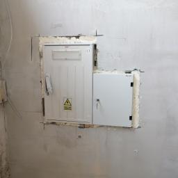 Elstart usługi elektryczne Michał Bejger - Dwie białe skrzynki elektryczne zamontowane w ścianie w trakcie prac wykończeniowych, widoczne ślady po ołówku i pianka montażowa wokół skrzynek.