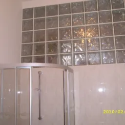 Łazienka z kabiną prysznicową i ścianą z luksferów, widok na fragment ściany i kabinę, wykonana w jasnych barwach.