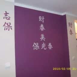 Fioletowa ściana z białymi, pionowo ułożonymi chińskimi znakami, ozdobne wnęki z oświetleniem i dekoracjami, białe ściany boczne z dodatkowymi znakami i włącznikiem światła.