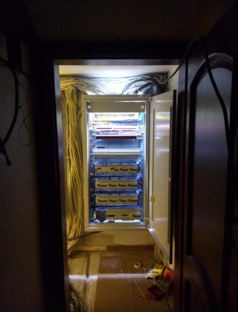 Otwarta szafa sterownicza z licznymi kablami i modułami, widoczna w ciemnym pomieszczeniu podczas montażu, z narzędziami leżącymi na podłodze.