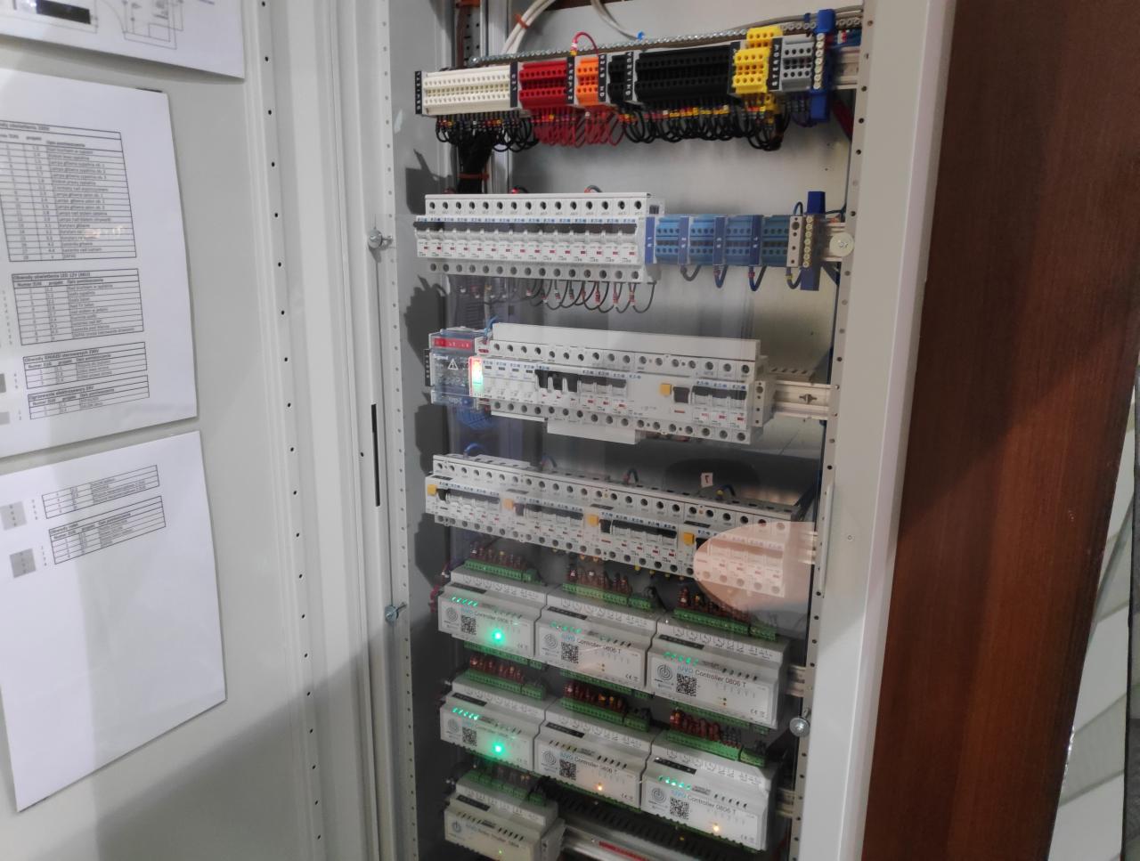Otwarta szafa sterownicza z elementami instalacji elektrycznej i automatyki, widoczna dokumentacja na drzwiach, Szczecin.