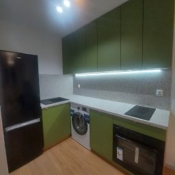 Firma Handlowo Usługowa Meblo-Man Krystian Babiarz - Nowoczesna kuchnia w odcieniach zieleni z czarnym sprzętem AGD: lodówka i piekarnik. Blat z motywem lastryko, oświetlenie LED pod szafkami wiszącymi, pralka w zabudowie.