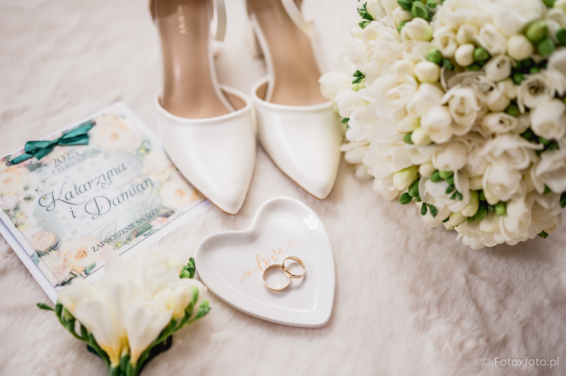 Eleganckie buty ślubne, bukiet z białych frezji, zaproszenie na ślub Katarzyny i Damiana oraz złote obrączki na talerzyku w kształcie serca.