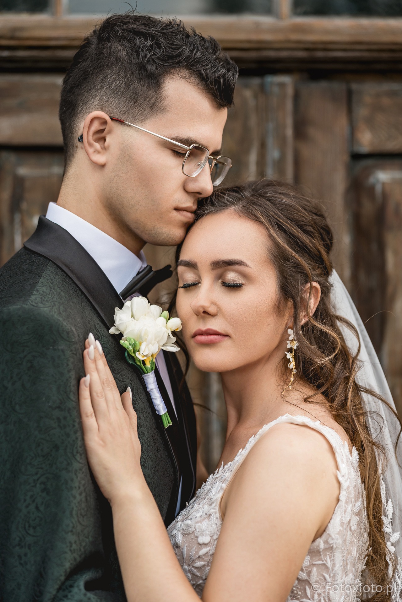 Romantyczne ujęcie pary młodej w Jarosławiu: Pan młody w ciemnozielonym smokingu i Panna Młoda w białej sukni ślubnej, delikatny makijaż i kwiaty.