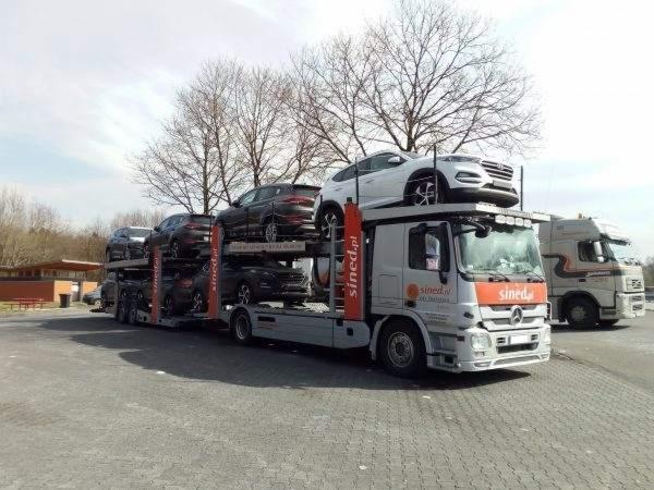 Laweta z załadowanymi samochodami marki Hyundai, widoczne logo firmy transportowej Sined.pl na boku pojazdu, na parkingu.