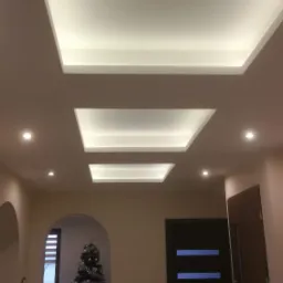 Sufit podwieszany z oświetleniem LED w kształcie trzech kwadratów, widoczne również drzwi wewnętrzne z przeszkleniami i choinka w tle.