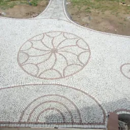 Wykończona nawierzchnia z jasnoszarej kostki granitowej z dekoracyjnymi elementami w kolorze ceglastym, tworzącymi wzory koła i półkola.