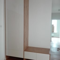 SCHAFFERMAN - szafy na wymiar - Szafa w przedpokoju z białymi, lakierowanymi frontami na wysoki połysk, drewnopodobnym korpusem i wbudowaną niską szafką z siedziskiem, z widoczną częścią podłogi z paneli.