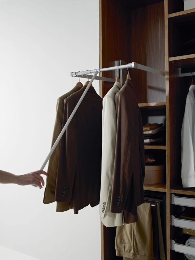 Wysuwany drążek na ubrania w szafie wnękowej z drewnianymi półkami i szufladami, widoczna dłoń obsługująca mechanizm.