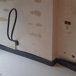 Bohdan - Wnętrze w trakcie prac wykończeniowych, widoczne przewody elektryczne wystające ze ściany, otwory na gniazdka i listwy przypodłogowe z pianki.