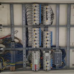 Bohdan - Otwarta skrzynka elektryczna z zamontowanymi bezpiecznikami, przewodami i listwami zaciskowymi, widoczne elementy marki Legrand i Schrack.