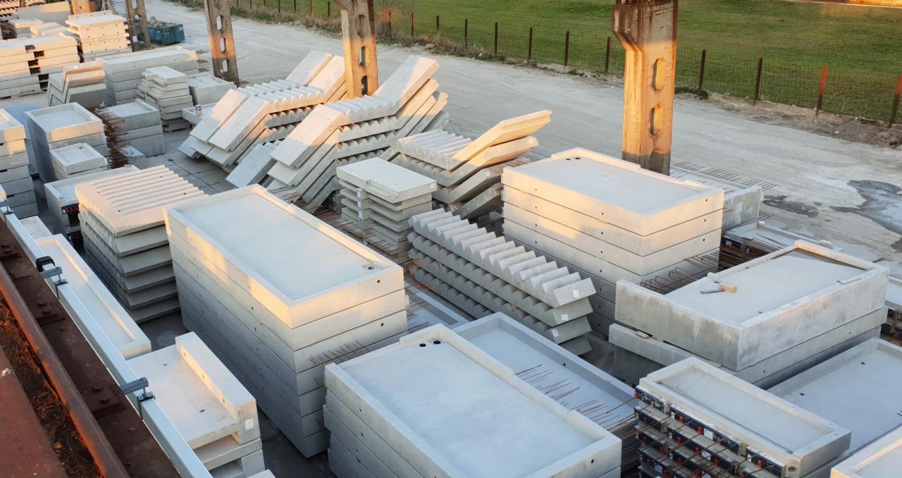 Magazyn prefabrykatów betonowych w Ozimku: stosy płyt, koryt i schodów betonowych w porannym słońcu.