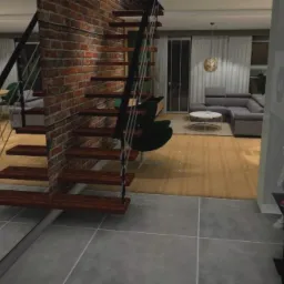 Wnętrze mieszkania z drewnianymi schodami na tle ceglanej ściany, widok na salon z szarą sofą i okrągłym stolikiem kawowym, nowoczesna lampka nocna na czarnym stoliku przy ścianie.