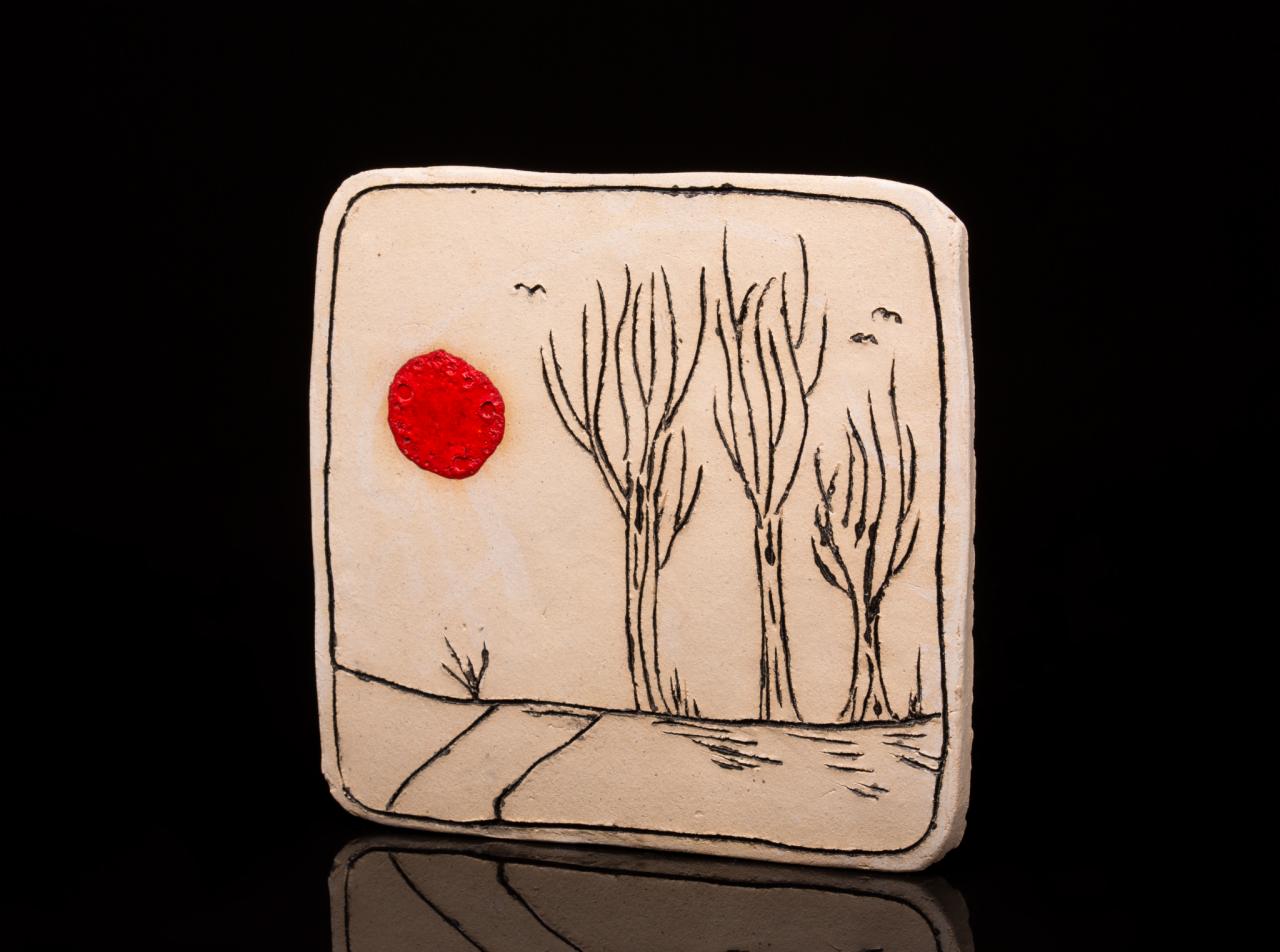 Ceramiczna płytka z ręcznie malowanym pejzażem: czerwone słońce, bezlistne drzewa i lecące ptaki na beżowym tle.