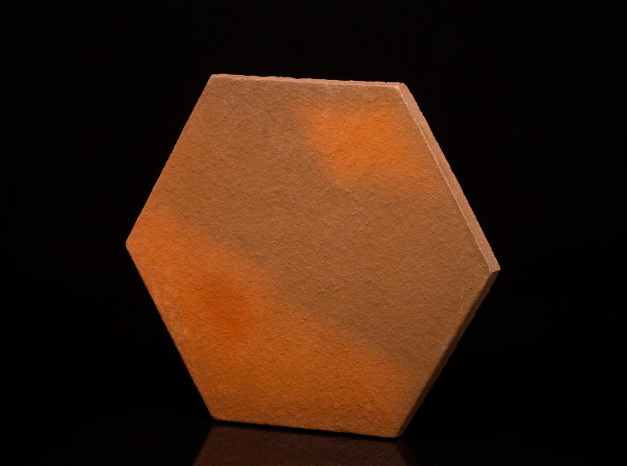 Heksagonalna płytka podłogowa w odcieniach brązu i pomarańczy na czarnym, błyszczącym tle, prezentująca teksturę i kolorystykę.