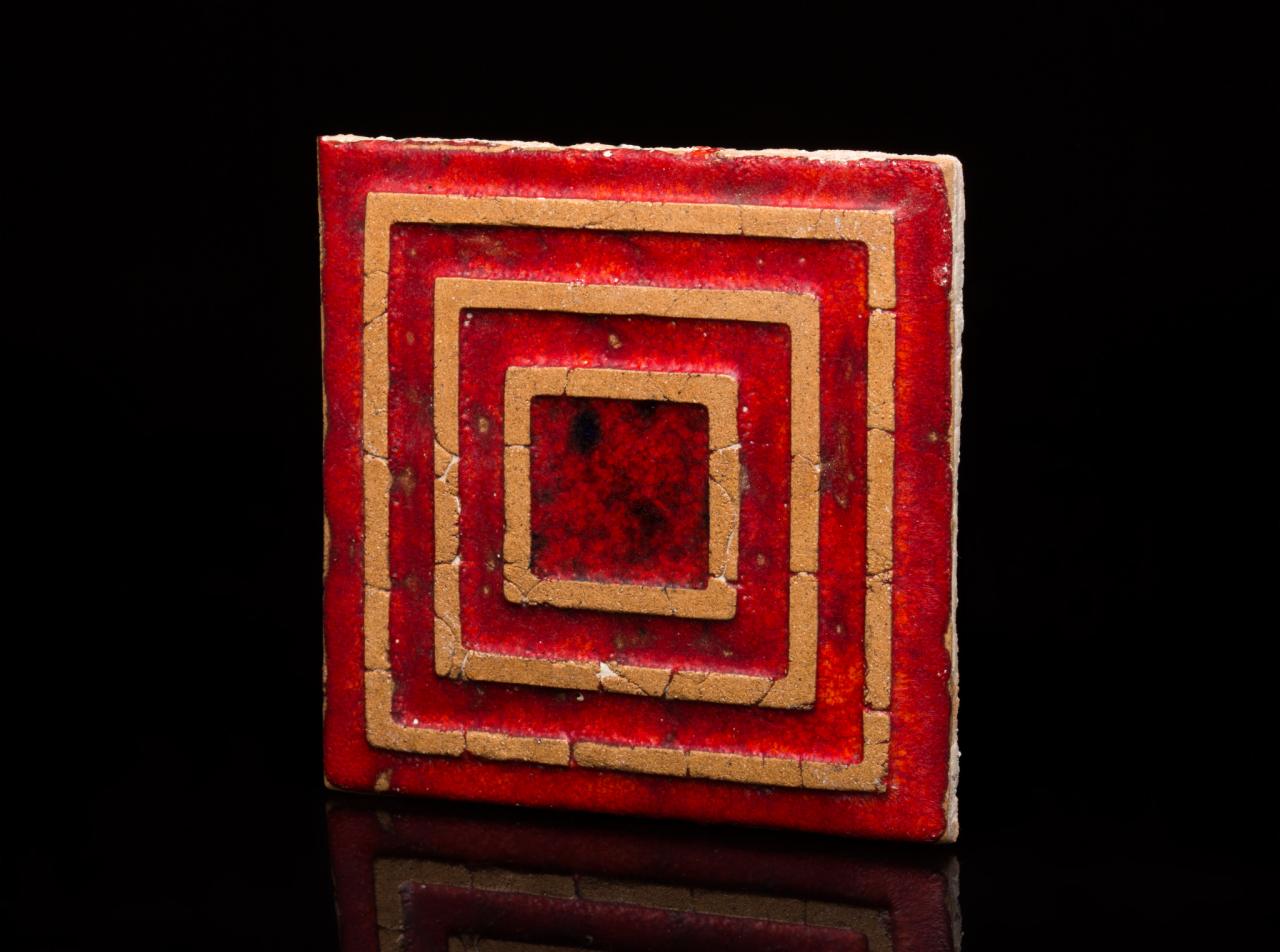 Czerwona, kwadratowa płytka ceramiczna z geometrycznym wzorem koncentrycznych kwadratów w odcieniach czerwieni i beżu, na czarnym, lustrzanym tle.